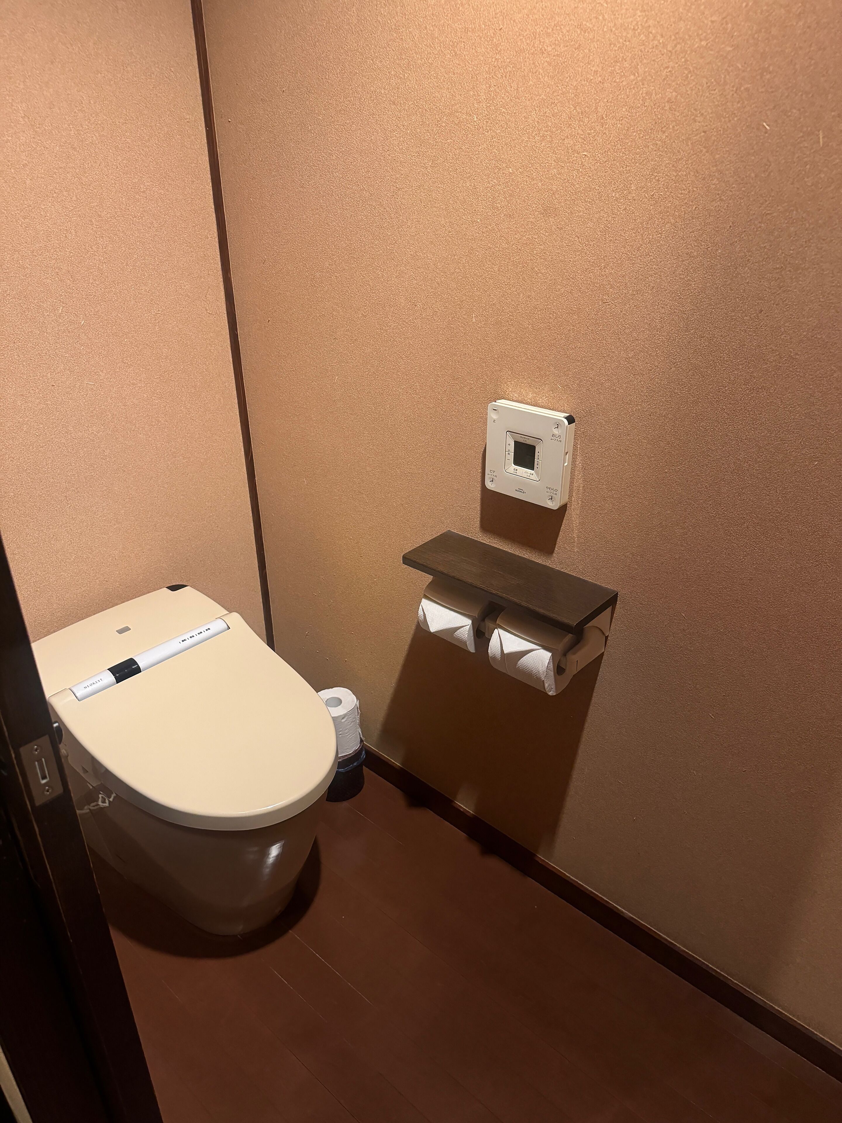 Een compacte, privé badkamer met toilet, een papieren handdoekdispenser en een prullenbak.