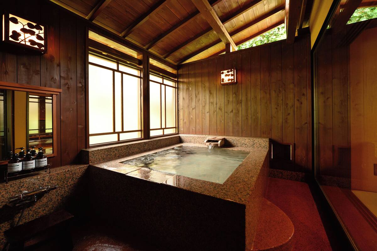 Un onsen japonais traditionnel, avec un intérieur en bois, un bain d’eau chaude et un banc en pierre.