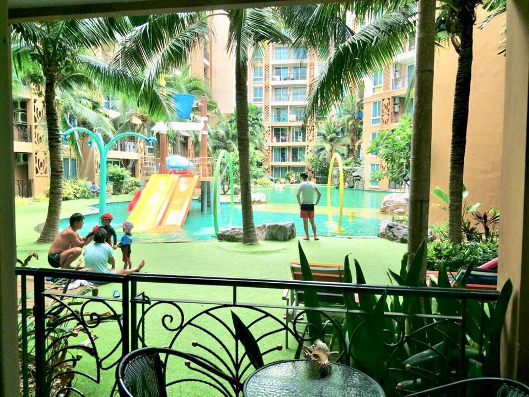 A pool area with a slide, palm trees, and a person standing by the pool.