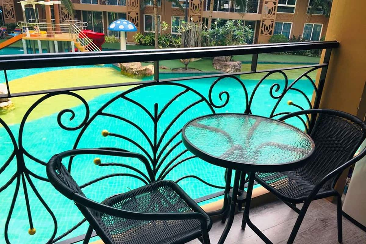 A balcony with a pool view, featuring a round glass table and two wicker chairs.