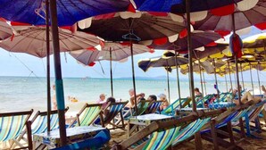 Un espace aménagé avec des sièges près de la plage, comprenant des chaises longues à rayures et des parasols colorés pour offrir de l’ombre.