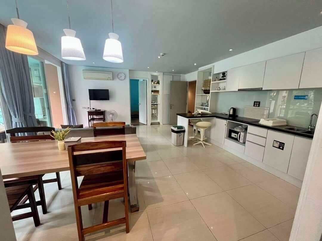 Une cuisine moderne avec des meubles blancs, un coin repas doté d’une table et de chaises en bois, et un éclairage suspendu.