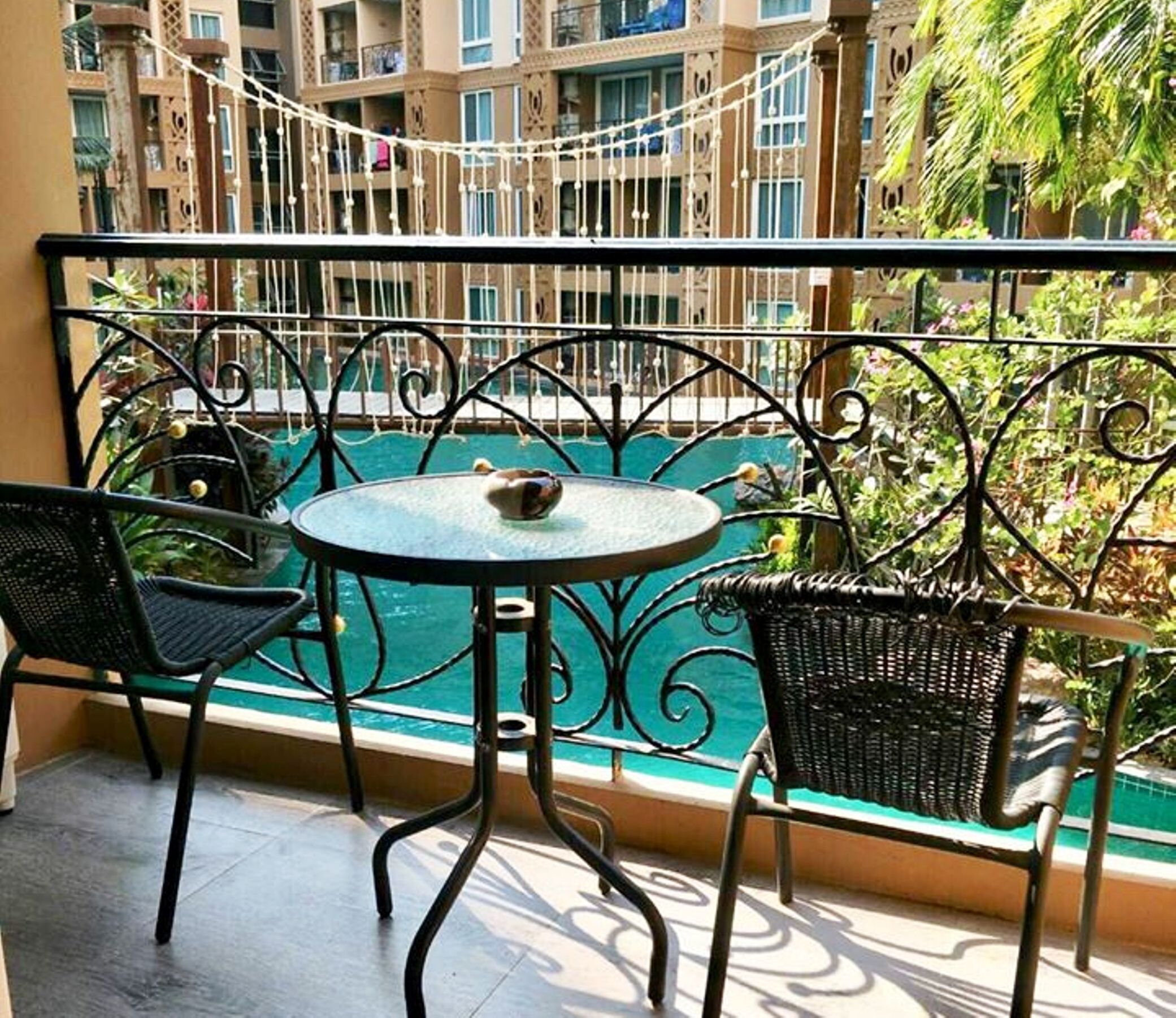 A balcony with a round table and two chairs, overlooking a swimming pool.