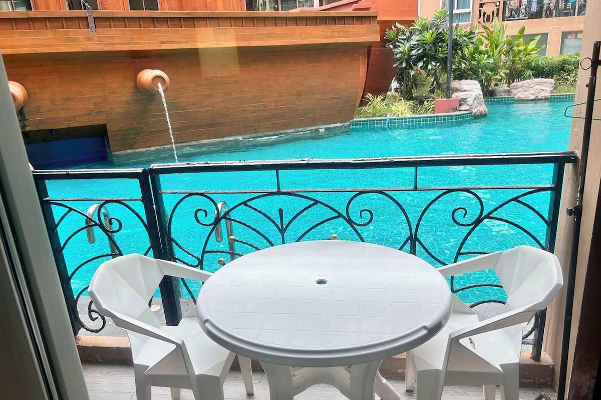 A balcony with a view of a swimming pool, white outdoor furniture, and a brick wall.