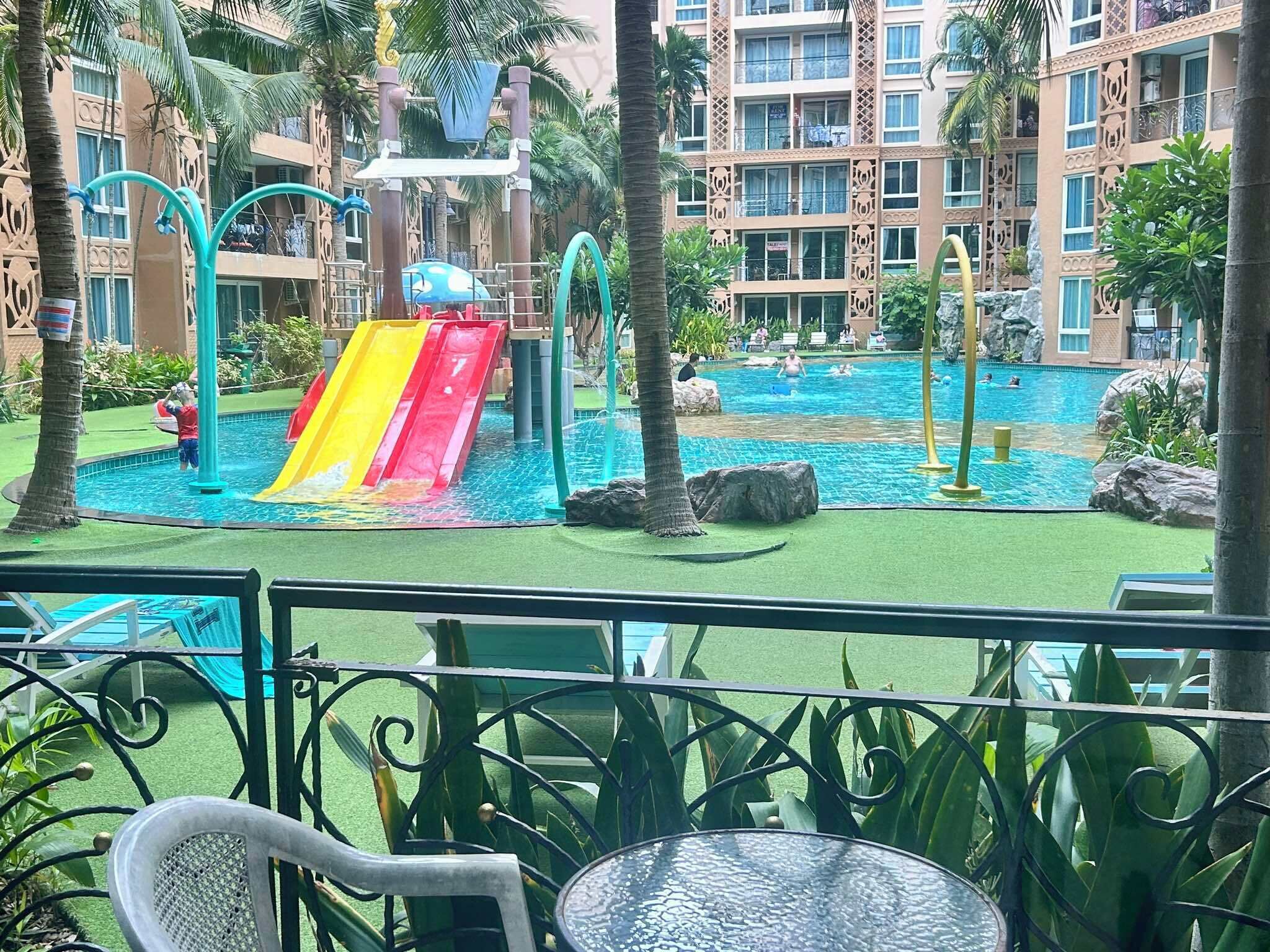 A pool area with a slide, palm trees, and a view of a hotel building.