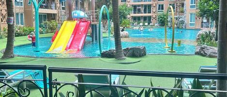 A pool area with a slide, palm trees, and a view of a hotel building.