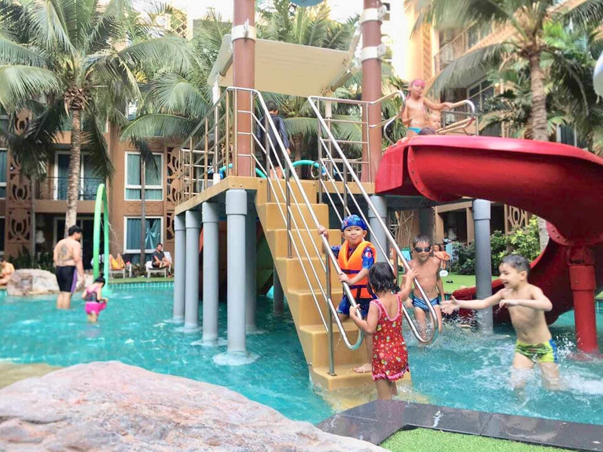Ein Wasserpark mit Rutsche, Klettergerüst und Poolbereich, umgeben von Palmen.