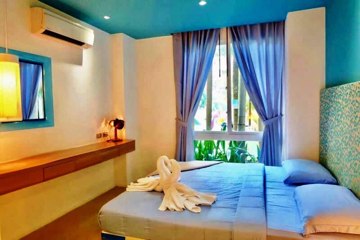 A hotel room with a bed, a bedside table, a lamp, and a window with curtains.