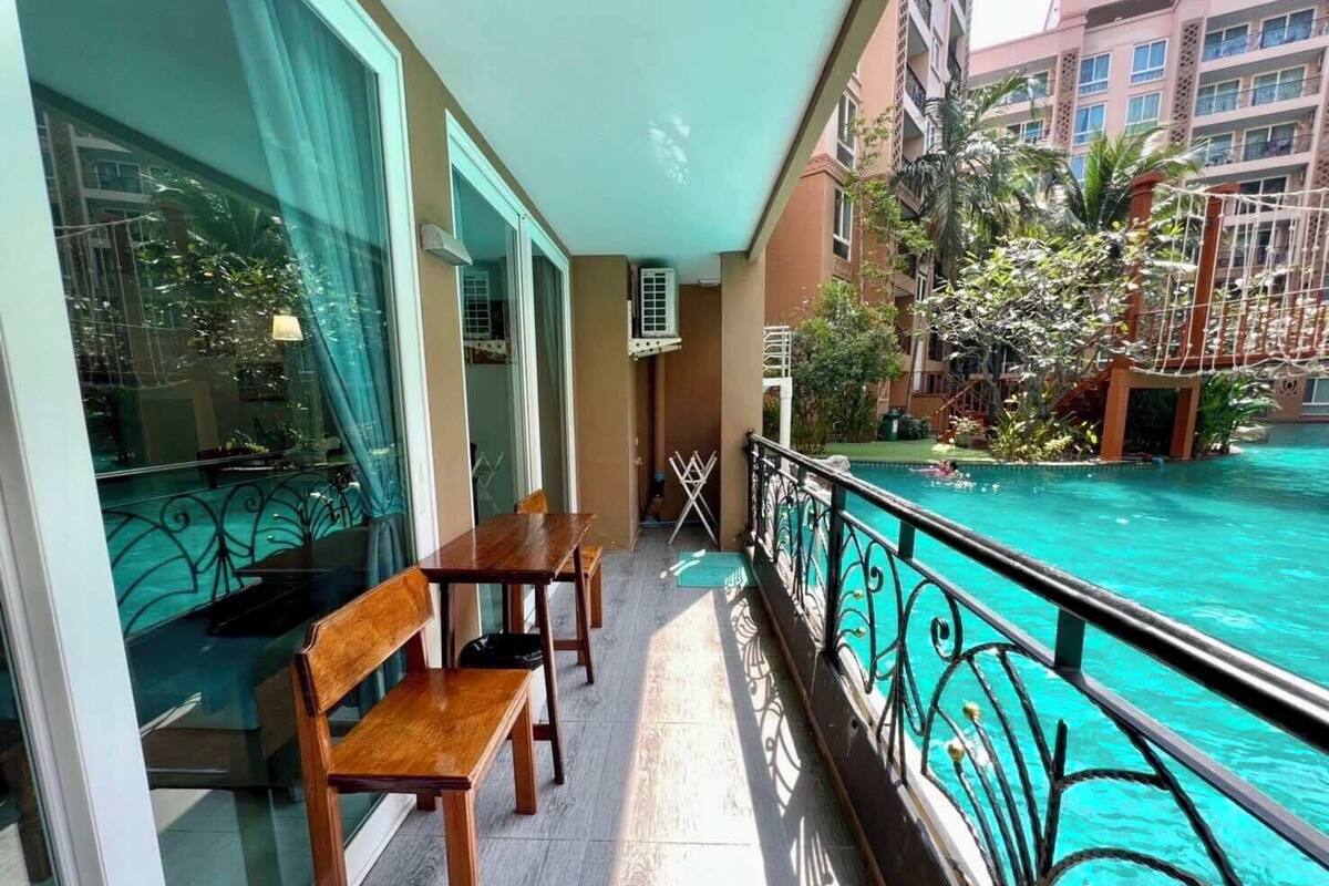 A balcony with a pool view, wooden furniture, and a railing.