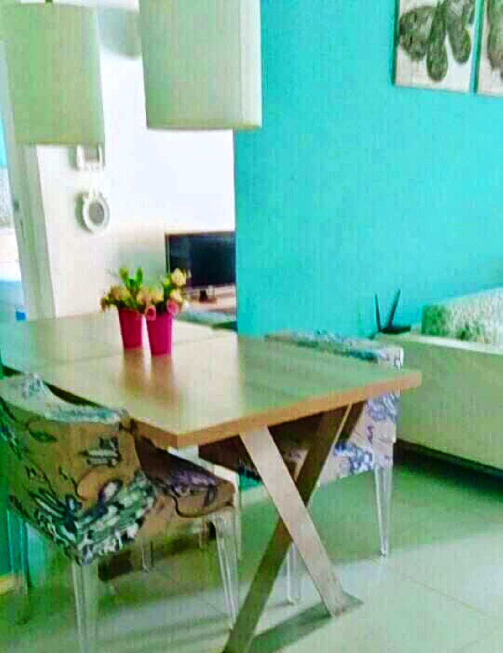 A dining area with a wooden table, clear chairs, and a teal-colored wall.
