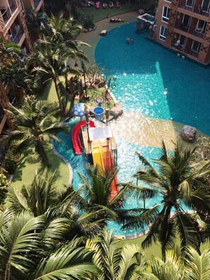A hotel pool area with a water slide, palm trees, and a building with balconies. - Atlantis Condo Pattaya by Panissara (Pattaya)