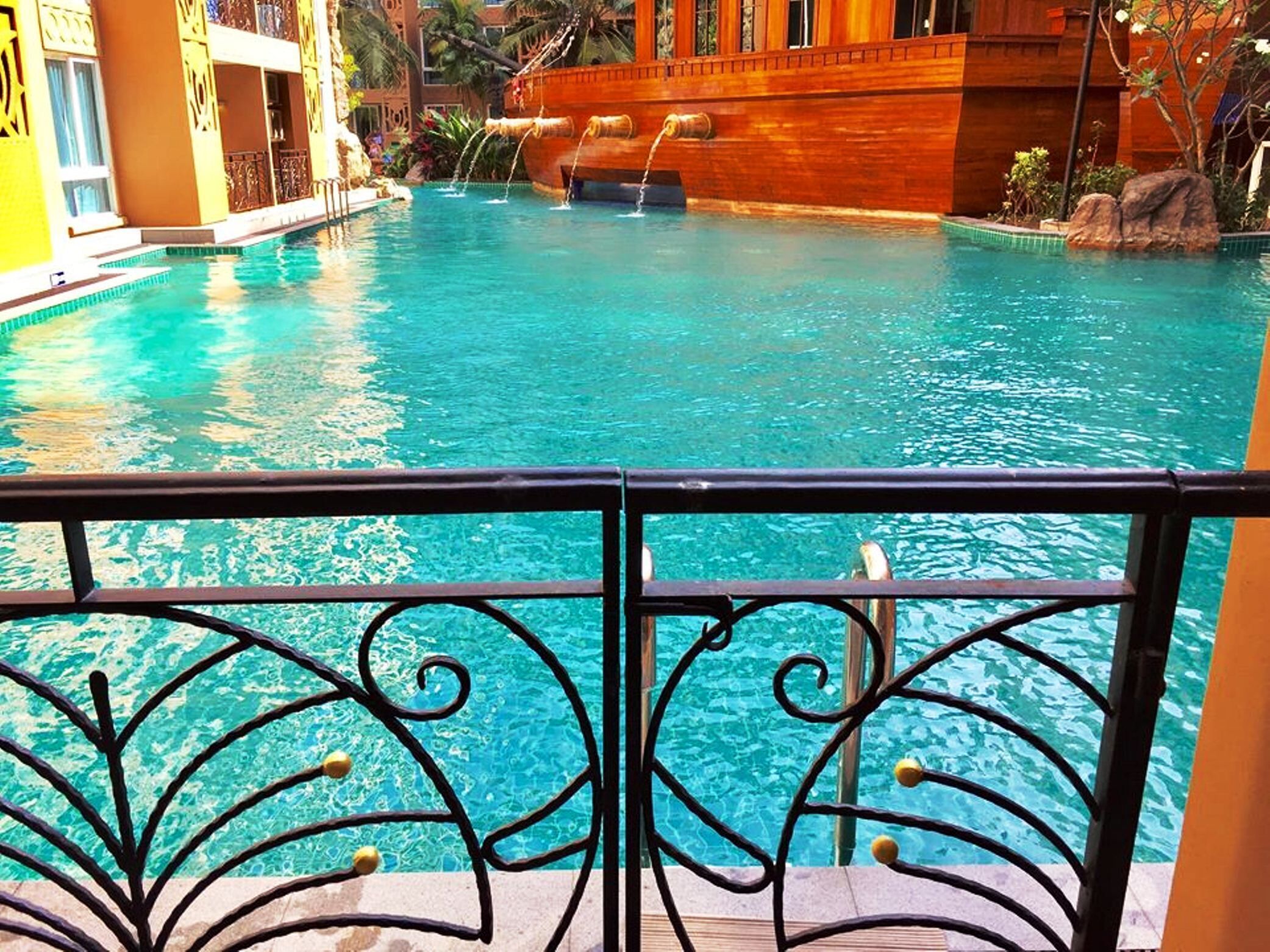A clear blue pool with a wooden boat structure in the background, surrounded by a yellow building with ornate railings.