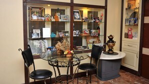A dining area with a glass table surrounded by chairs, a small island with a decorative item, and a view through a window displaying various personal items and decorations. - Best House Hotel (Alanya)