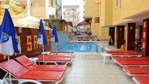 A poolside area with sun loungers and umbrellas, a tiled floor, and a view of the surrounding buildings. - Best House Hotel (Alanya)