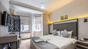 A modern hotel room with a large bed, a desk, a television, and a window with blinds. - Taksim Trust Hotel (Istanbul)