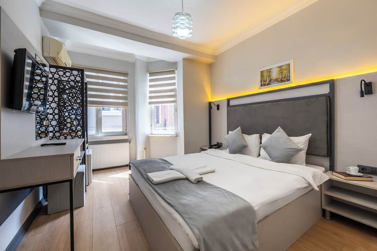 Ein modernes Hotelzimmer mit einem großen Bett, einem Schreibtisch, einem Fernseher und einem Fenster mit Jalousien.