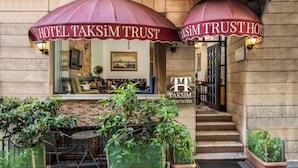 A hotel entrance with two large maroon umbrellas, a reception desk, and potted plants. - Taksim Trust Hotel (Istanbul)