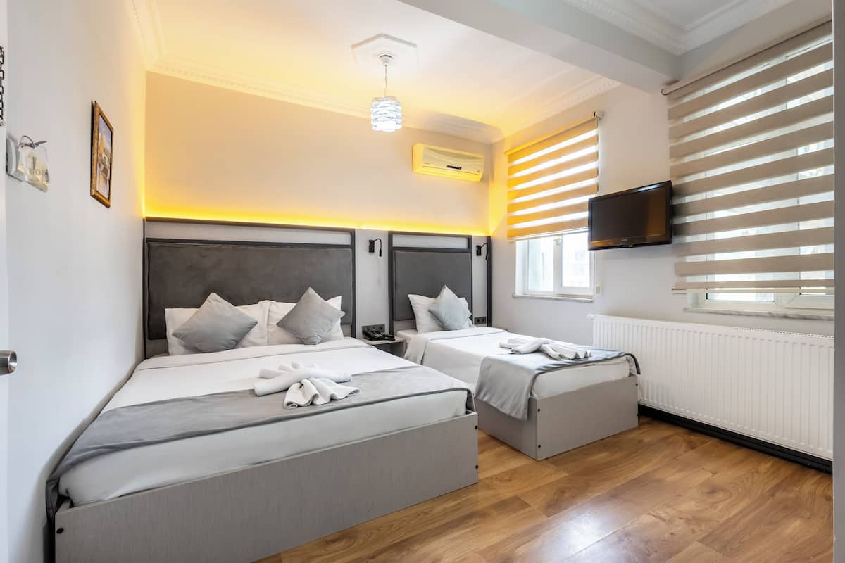 Ein Hotelzimmer mit zwei Betten, einem Flachbildfernseher, einem Fenster mit Jalousien und einer Deckenleuchte.