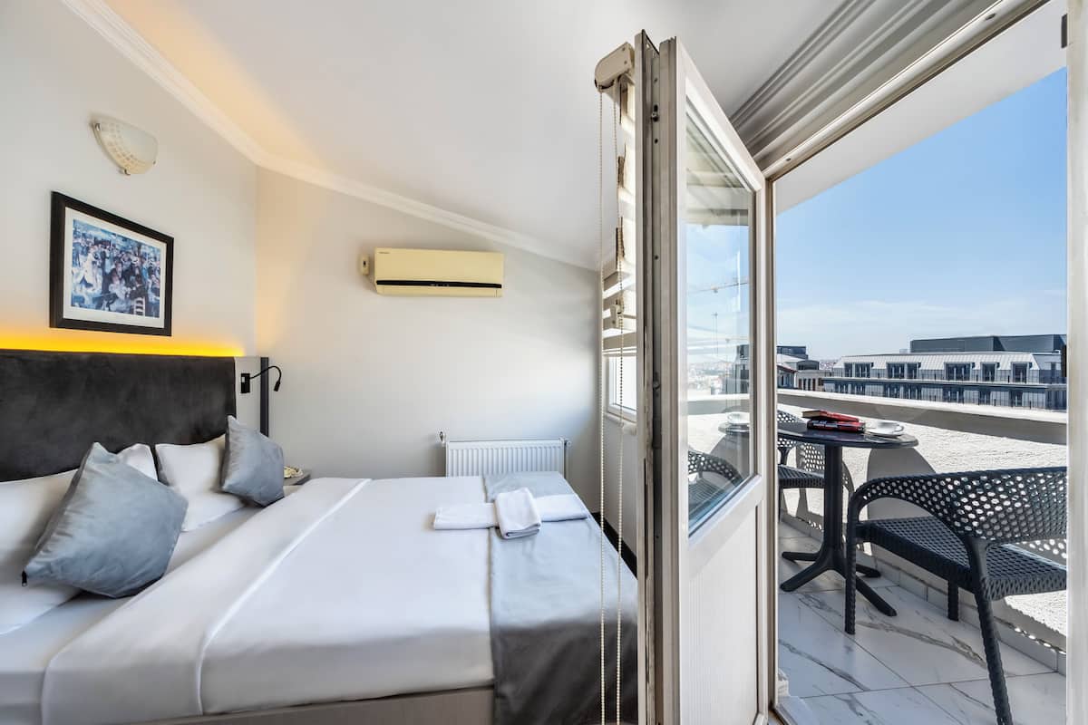 Ein Hotelzimmer mit Bett, Heizkörper, Klimaanlage, einem gerahmten Foto an der Wand und einem Balkon mit Tisch und Stühlen.