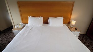 Una habitación de hotel con una cama grande, dos mesitas de noche y una lámpara.