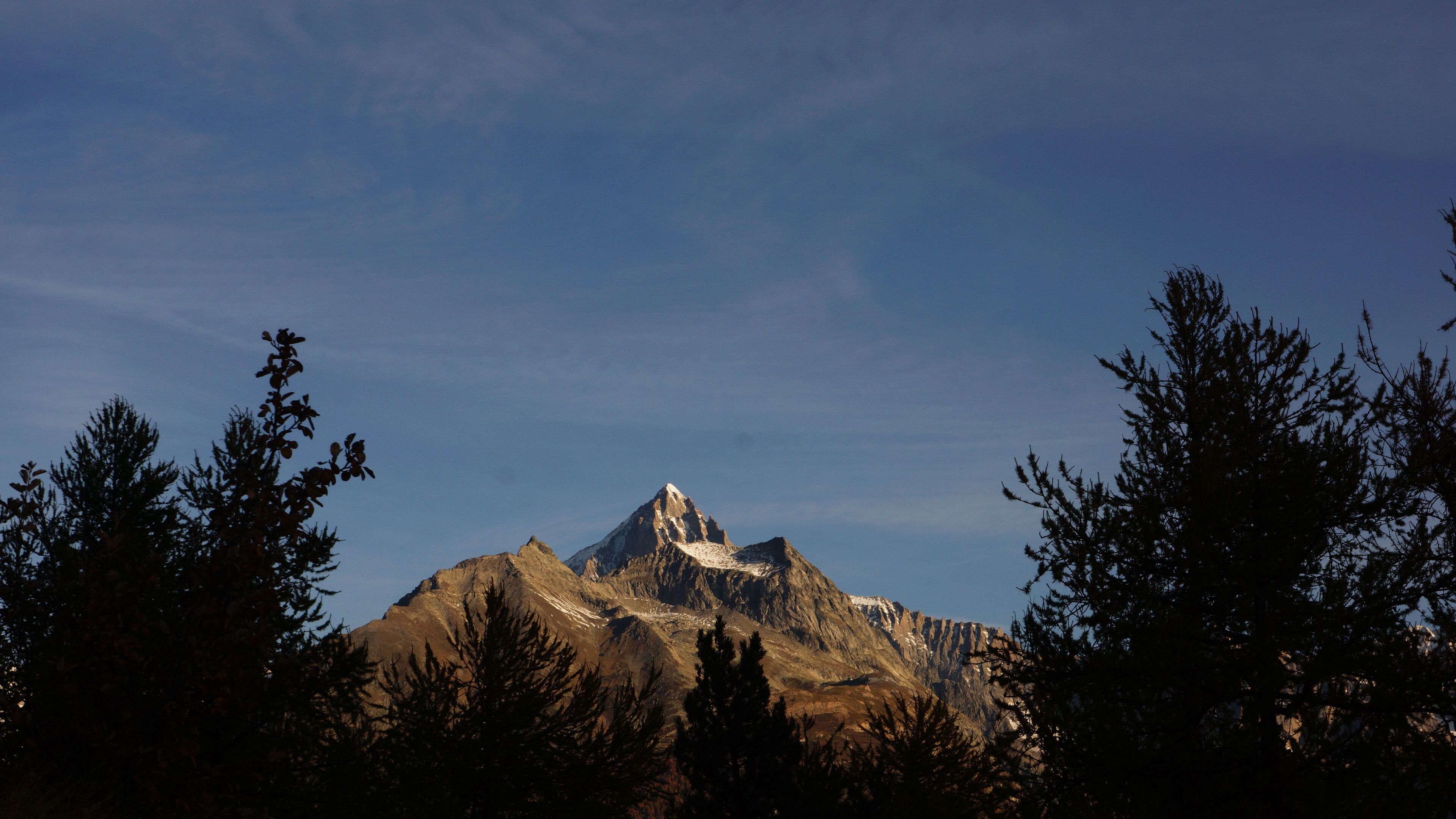 A mountain with a snow-capped peak, surrounded by trees.