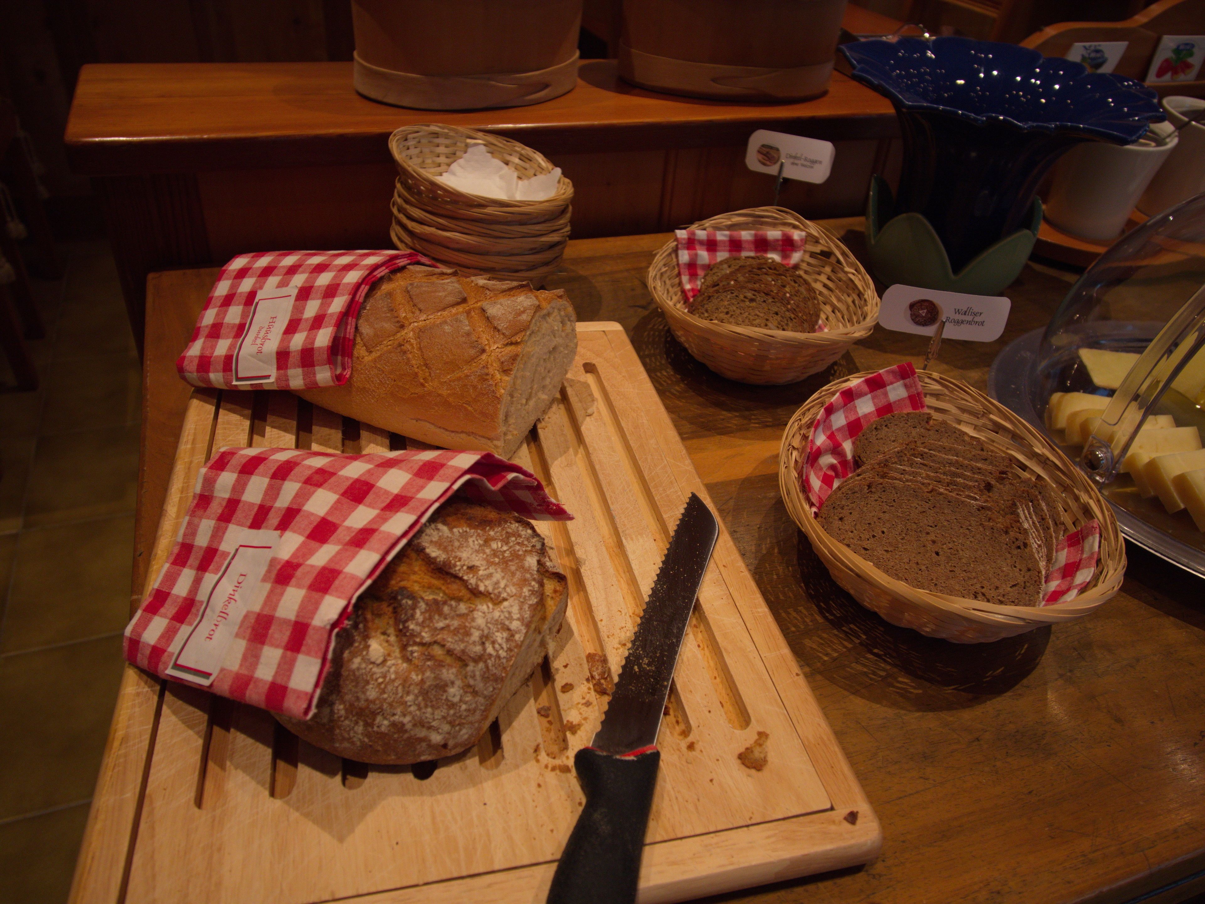 A bakery display with various breads and a cutting board with a knife.