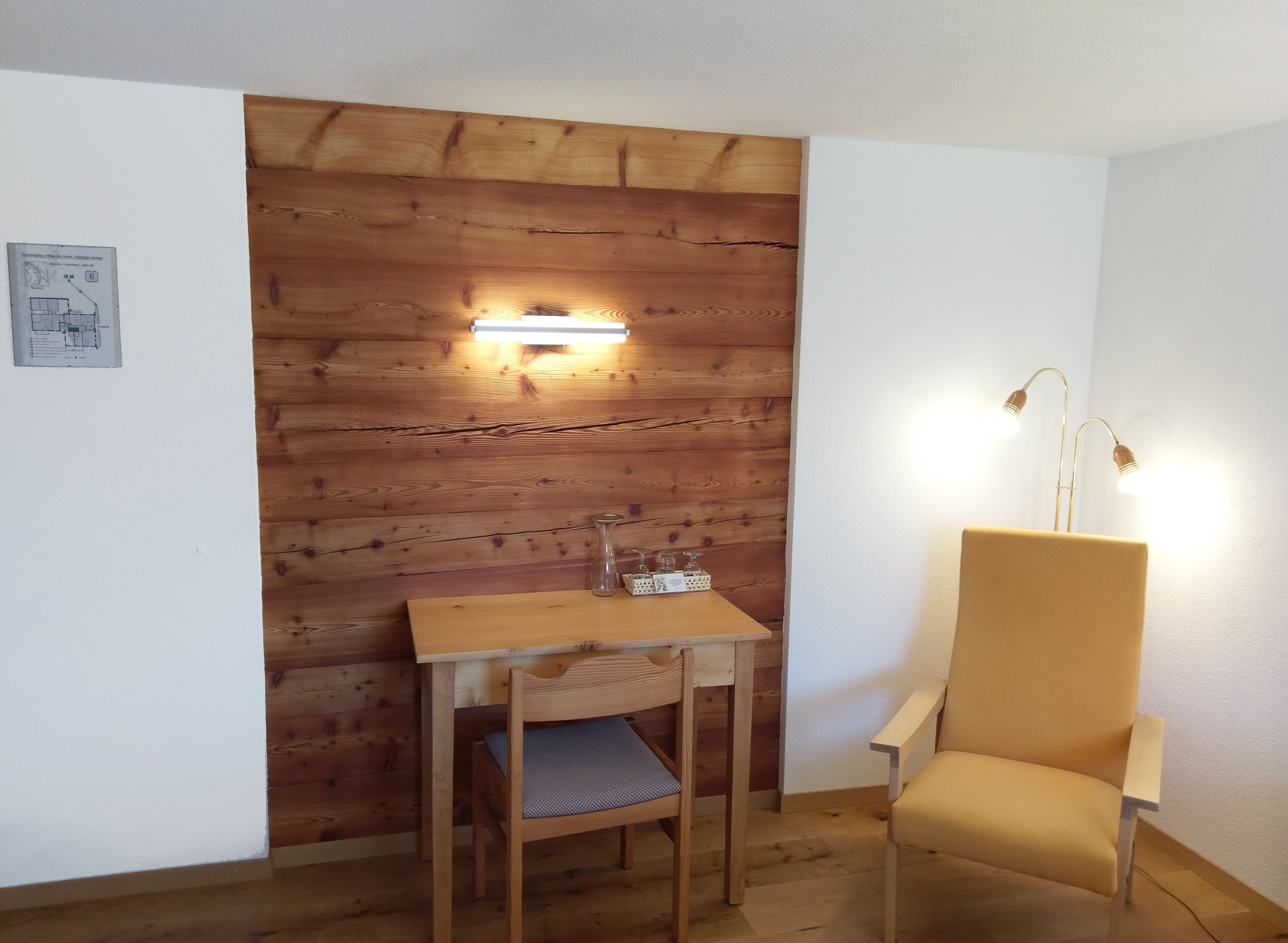 Una habitación pequeña con una pared de madera, una mesa con una silla y una lámpara.