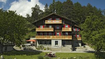 Un hotel a più piani con balconi, facciata in pietra e una zona giardino.