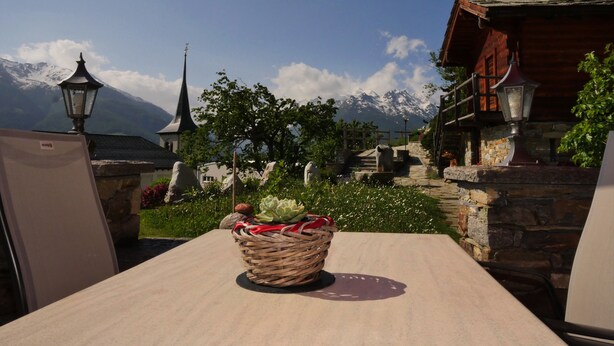 Una mesa con una cesta que contiene frutas y frutos secos, un paraguas rojo y una vista de una montaña e iglesia.