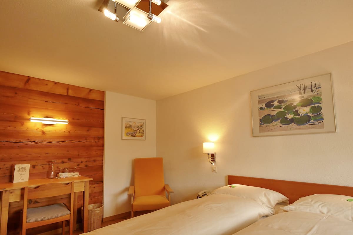 A hotel room with a wooden wall, a desk with a chair, a bed with white bedding, and two wall-mounted lights.