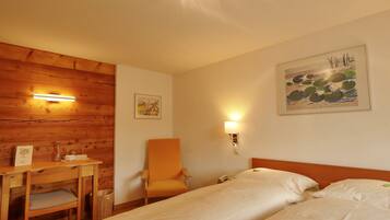 Ein Hotelzimmer mit Holzwand, Schreibtisch mit Stuhl, Bett mit weißer Bettwäsche und zwei Wandlampen.
