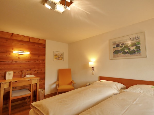 Habitación de hotel con pared de madera, un escritorio con silla, cama con ropa de cama blanca y dos luces fijadas a la pared.