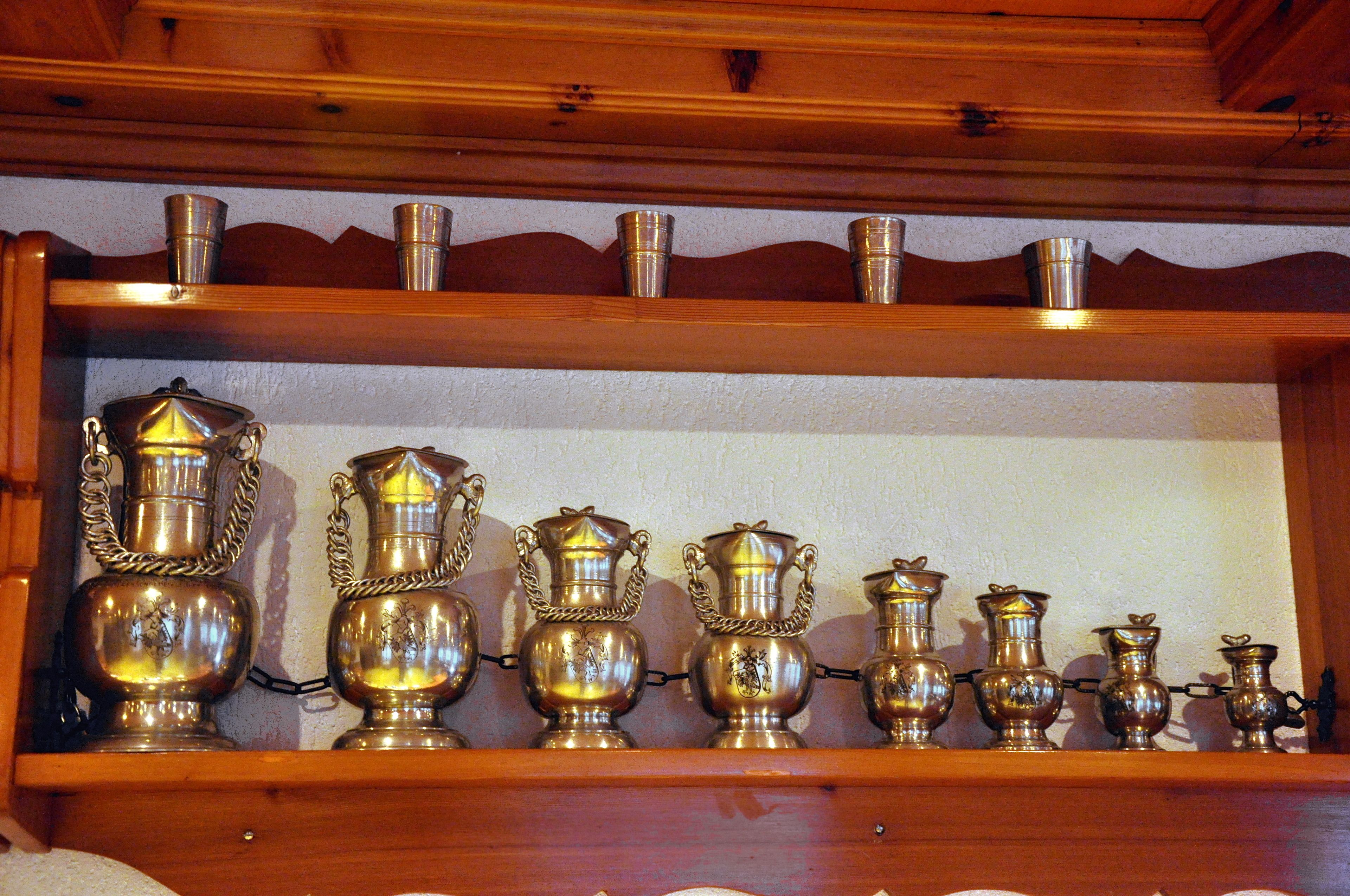 A wooden shelf with various metal containers, including a large jug with a handle and smaller pitchers.