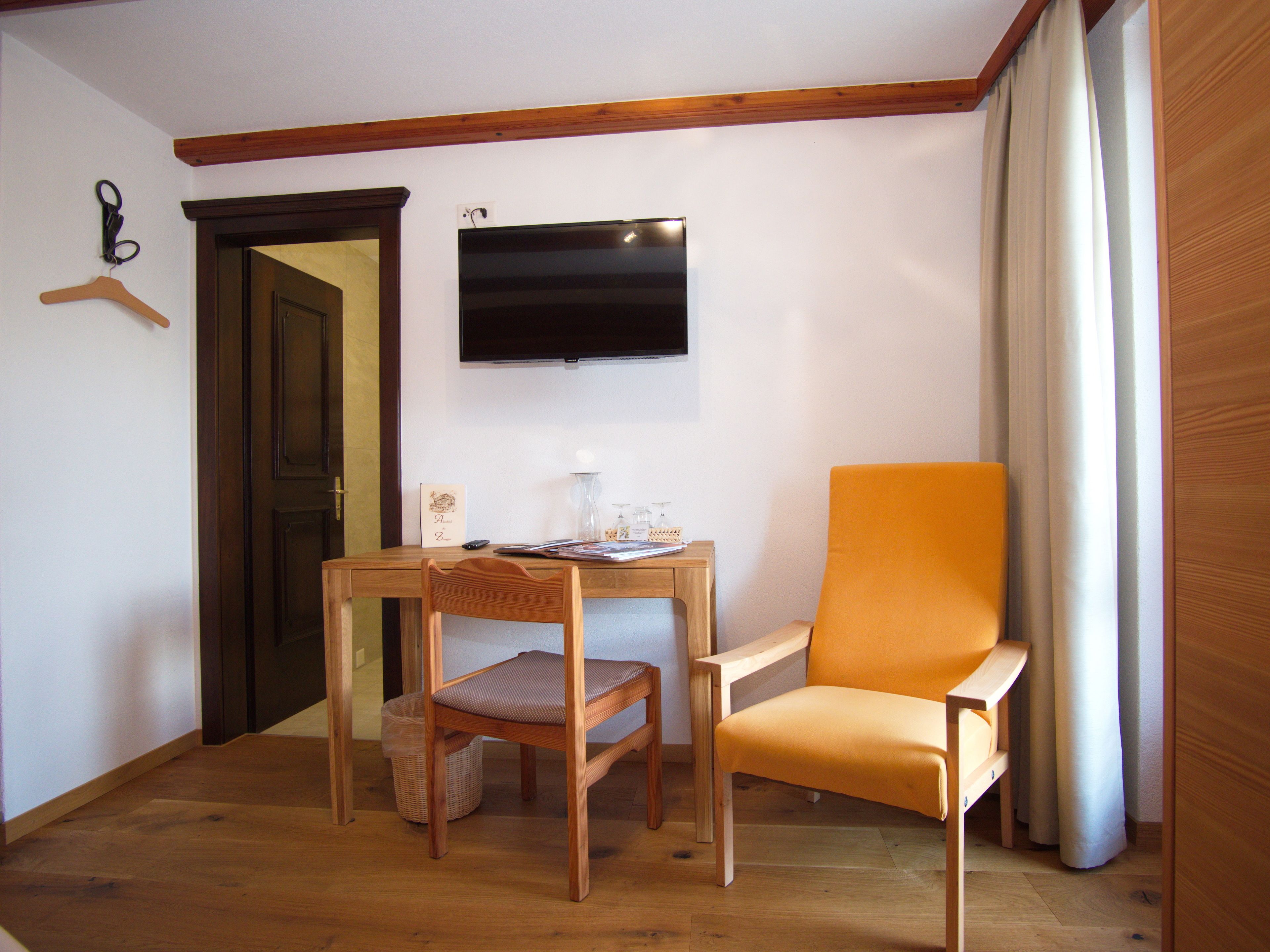 A room with a wooden table, two chairs, a TV mounted on the wall, and a door.