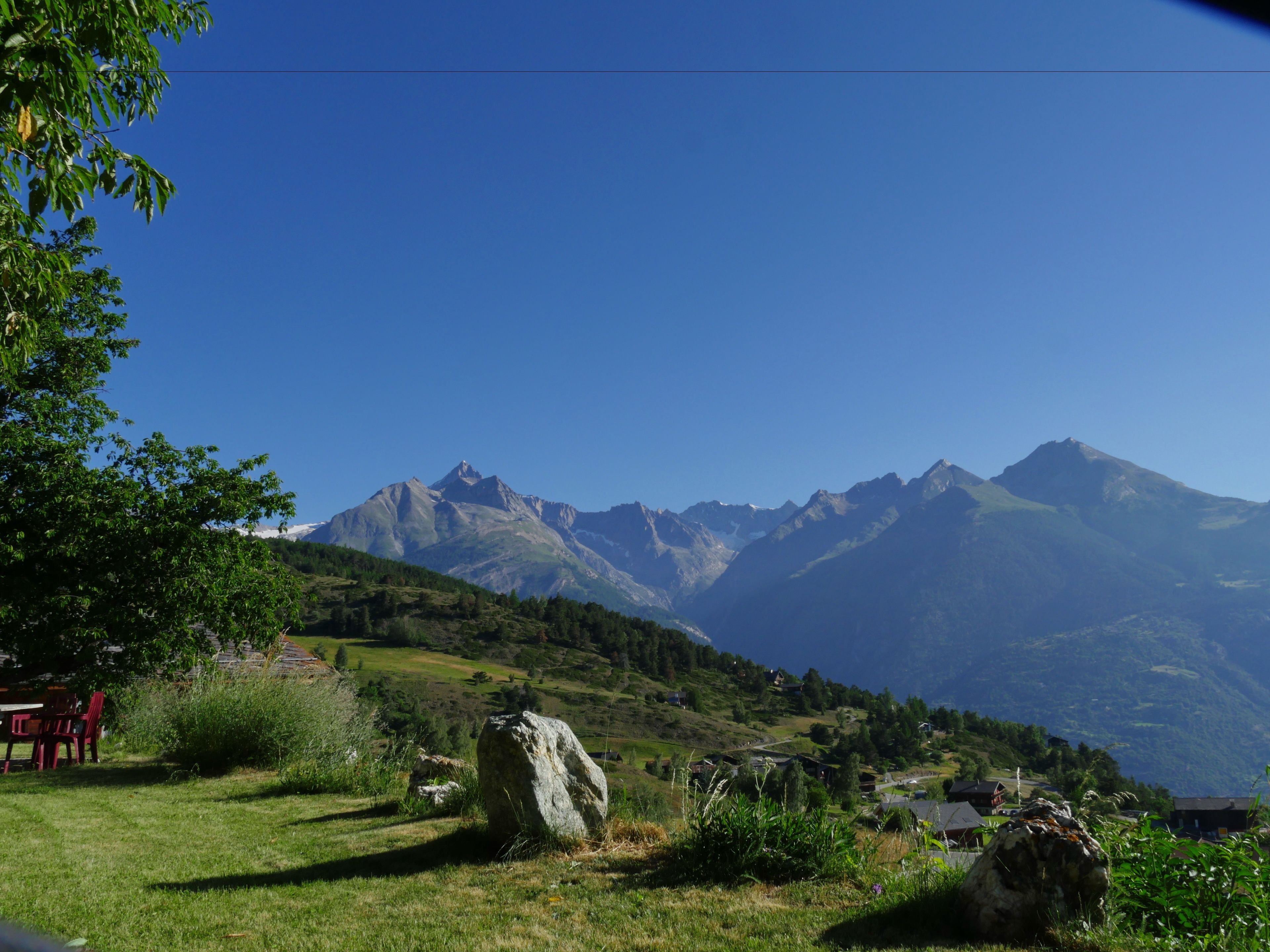 Un paisaje montañoso con cielo despejado, una roca grande al frente y algunas casas en el valle.