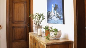 Una puerta de madera con un letrero encima, un aparador de madera con plantas, un cuadro en la pared y un techo de madera.
