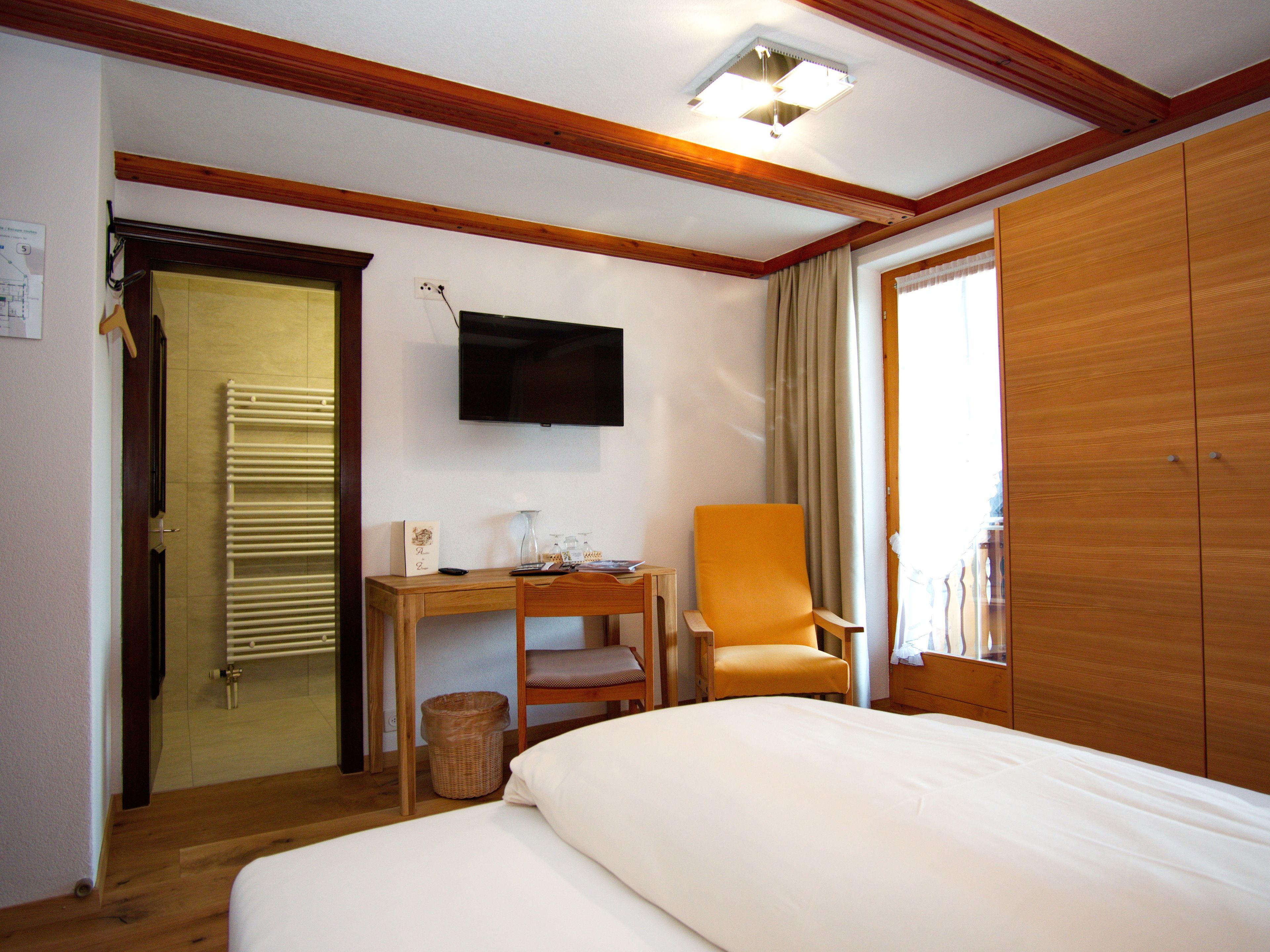 A hotel room with a bed, a desk, a chair, a television, and a wardrobe.