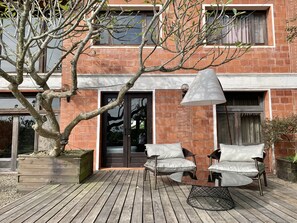 A modern building with a brick facade, a wooden deck with outdoor furniture, and a large tree in the foreground. - The One Nanyuan (Xinpu)