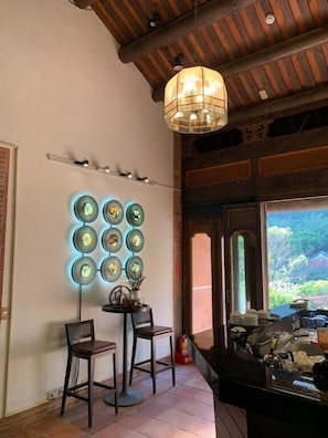A dining area with a wooden ceiling, a wall-mounted light fixture, and a view of greenery outside. - The One Nanyuan (Xinpu)