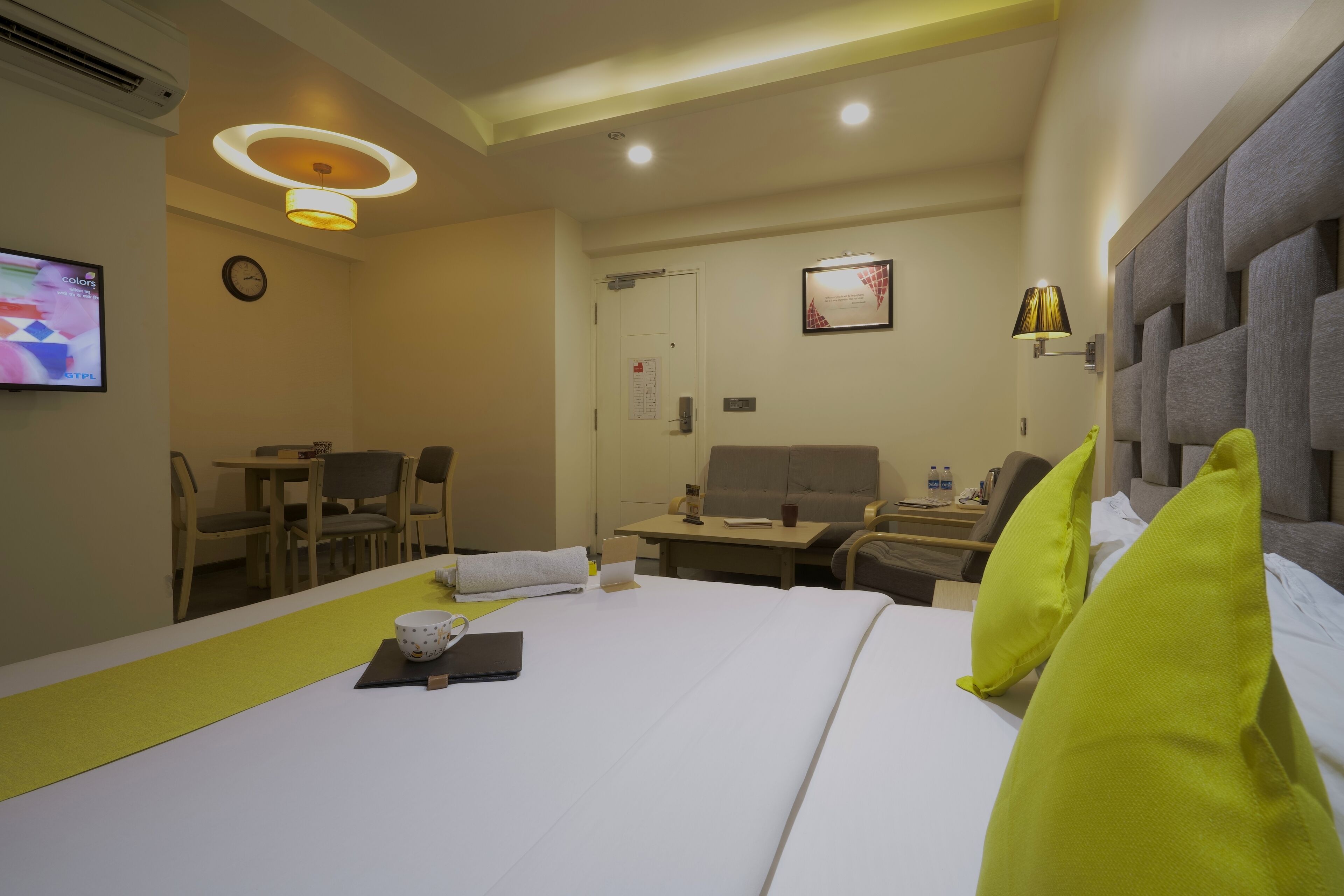 A hotel room with a bed, a desk, a chair, a television, and a wall-mounted clock.