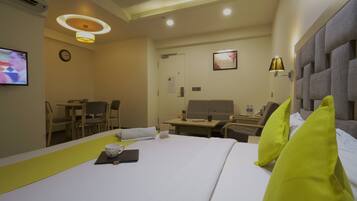 A hotel room with a bed, a desk, a chair, a television, and a wall-mounted clock.