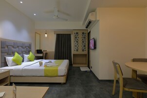 Una habitación de hotel con cama, escritorio, silla, televisor y una mesita.
