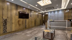 A lobby with wooden panel walls, a flat-screen TV, a reception desk, and a clock. - Hotel Sifat International (Surat)