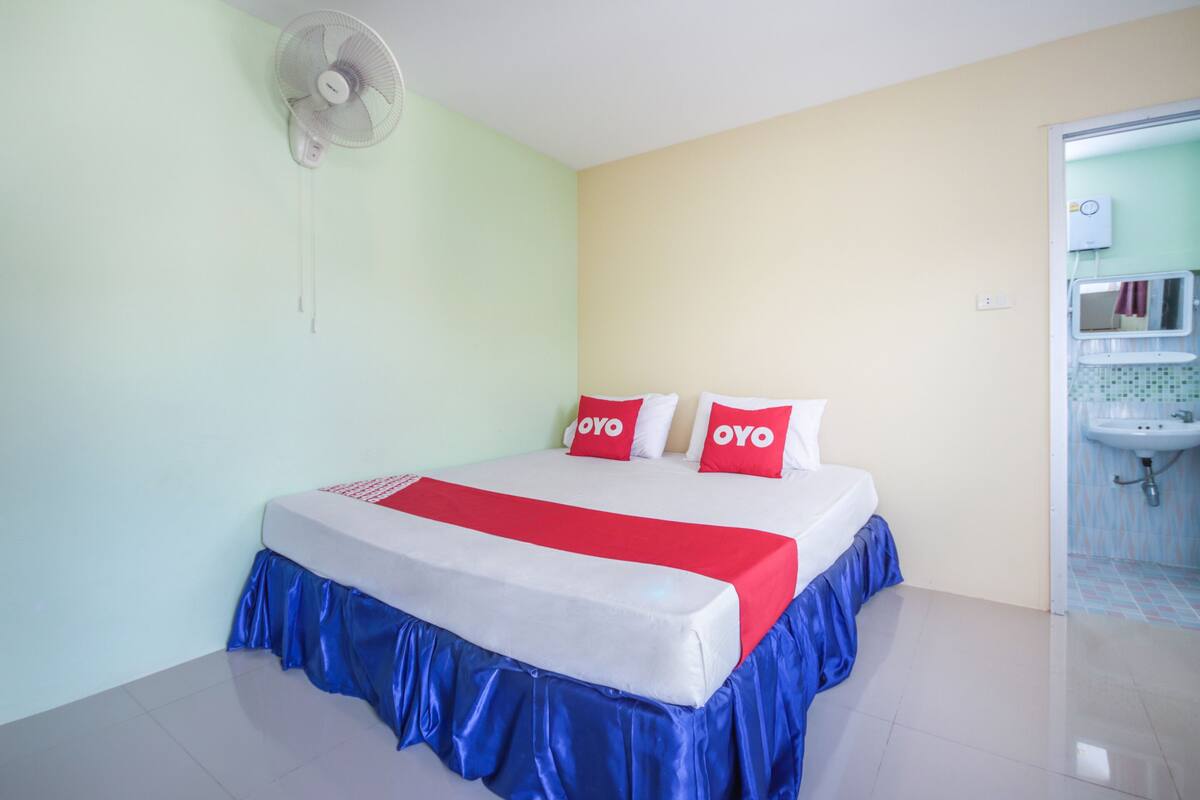 A hotel room with a bed, a fan, and a bathroom visible through an open door.