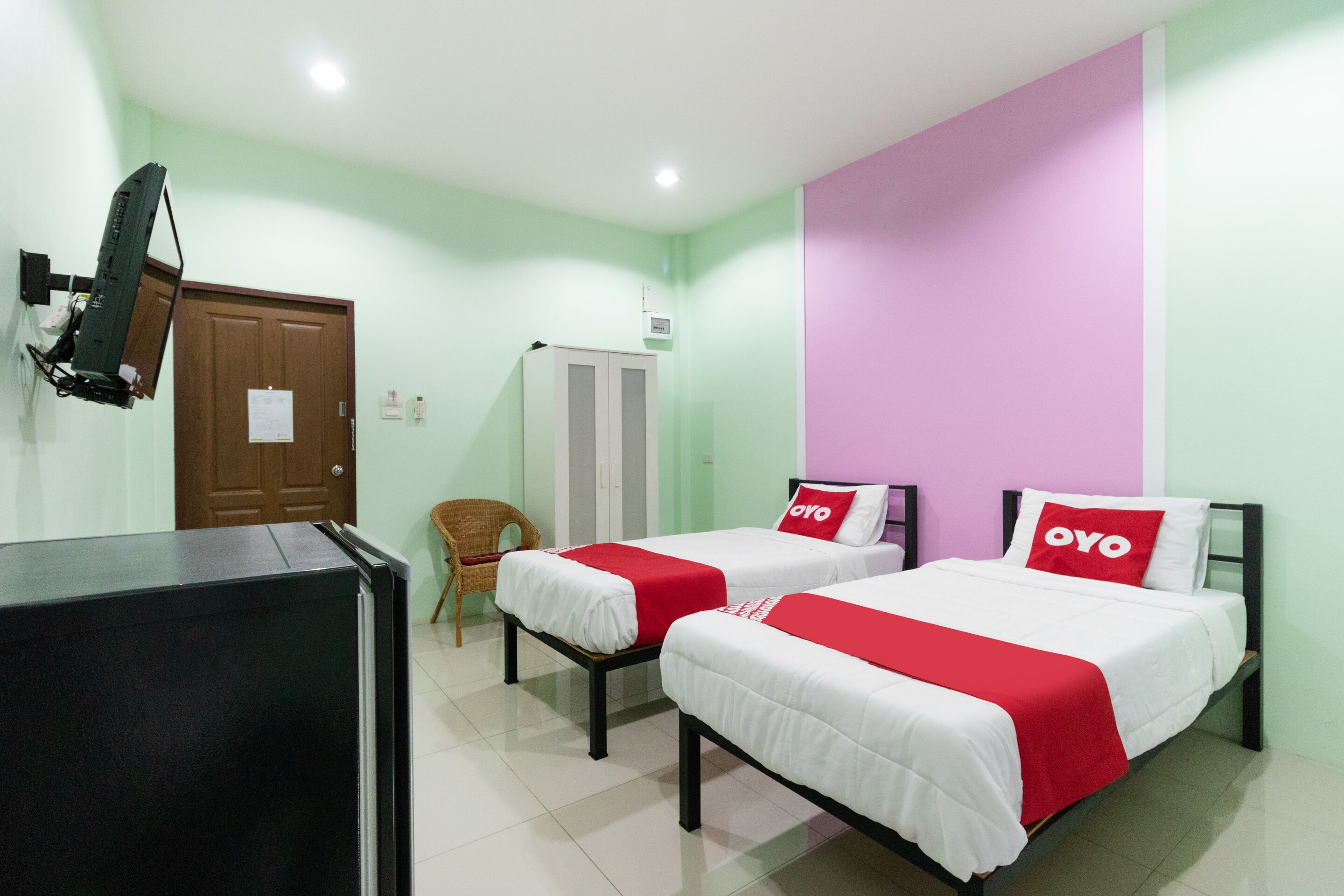 A hotel room with two beds, a TV, a wardrobe, and a chair.