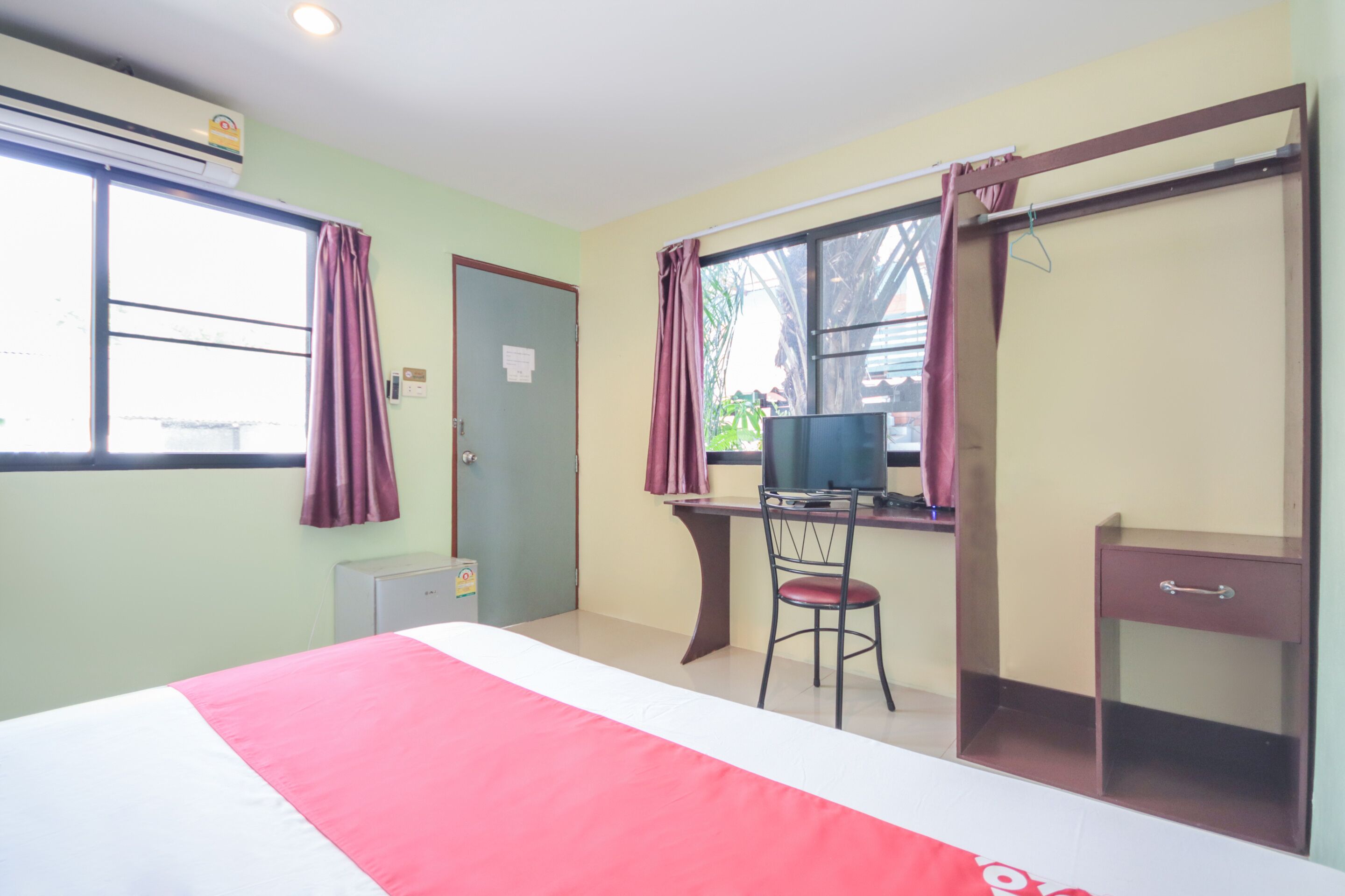 A hotel room with a bed, a desk with a chair, a television, a wardrobe, and a window with curtains.
