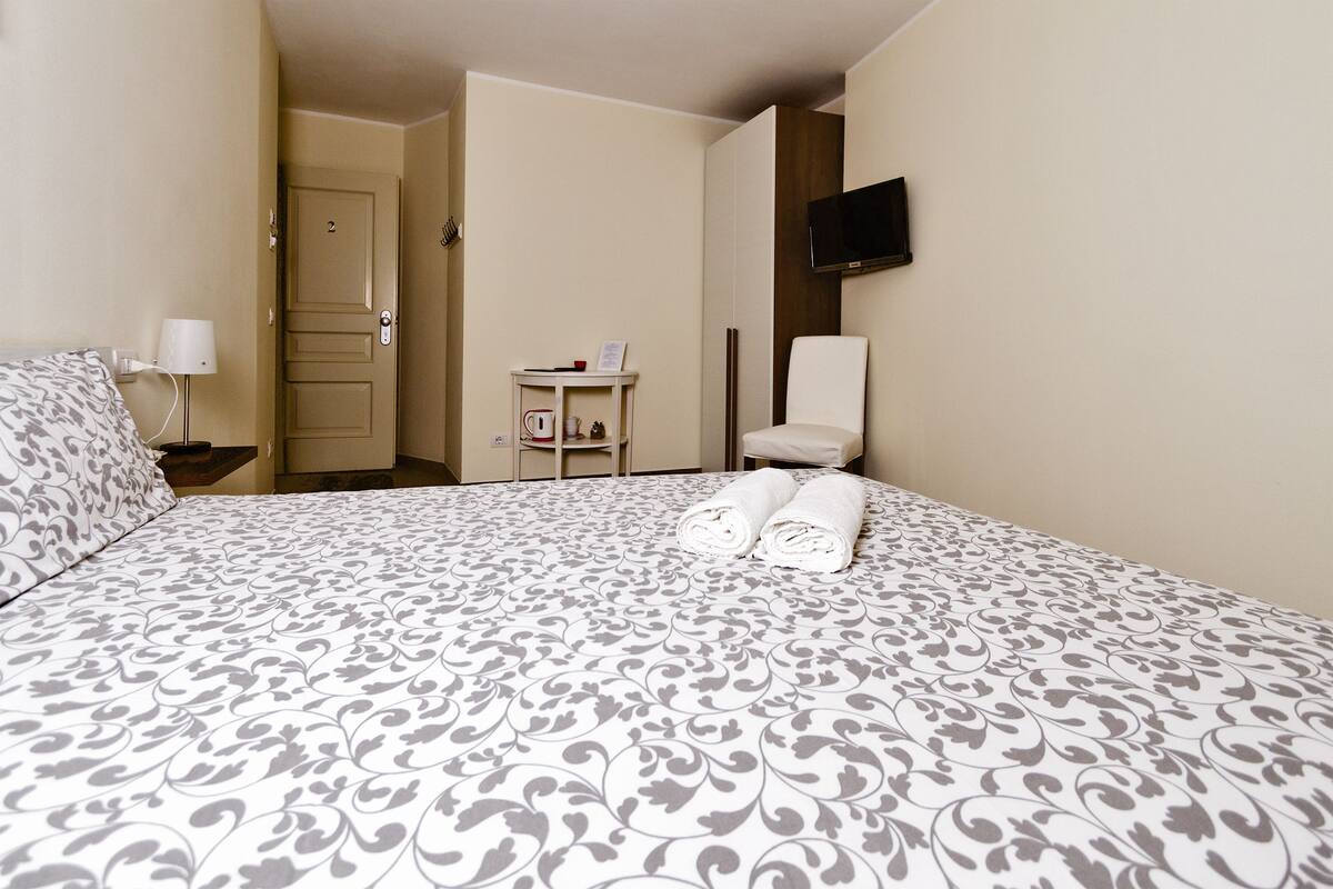 Ein Hotelzimmer mit Bett, Sessel, Fernseher und einem kleinen Tisch mit Lampe.