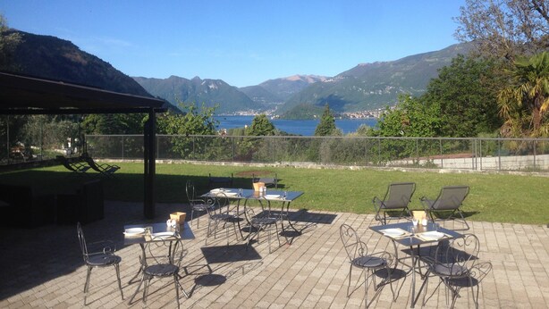Une terrasse extérieure avec des tables et des chaises, offrant une vue sur un lac et des montagnes.
