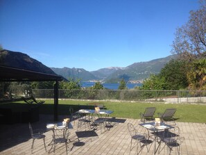 An outdoor patio with tables and chairs, overlooking a lake and mountains. - Andirivieni Bellagio Guest House (Bellagio)