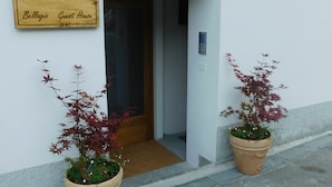L’entrée d’une maison d’hôtes, avec une enseigne en bois, deux plantes en pot et une porte donnant sur l’intérieur.